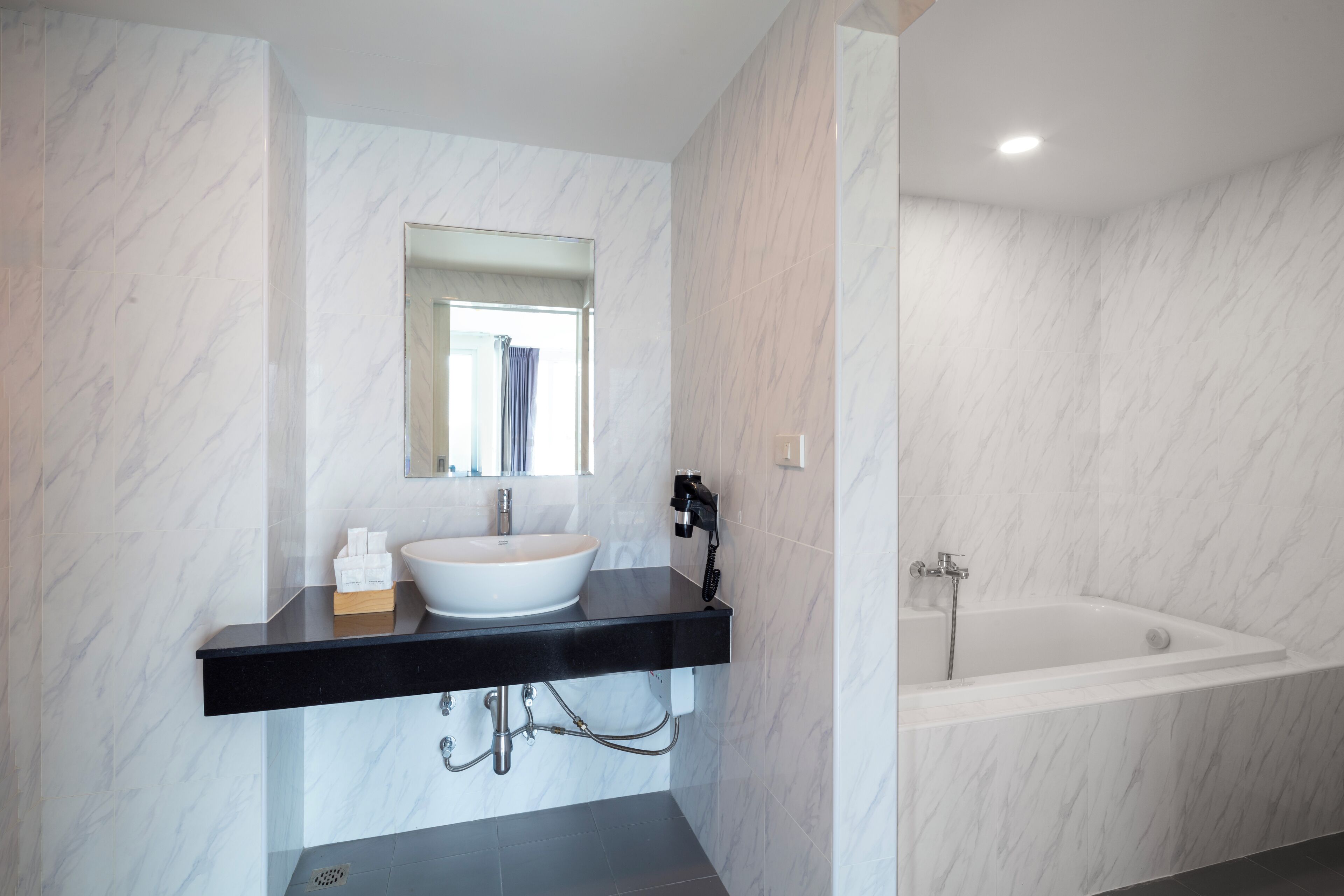 Une salle de bain moderne avec un lavabo en marbre blanc, un plan de toilette noir et une baignoire blanche.
