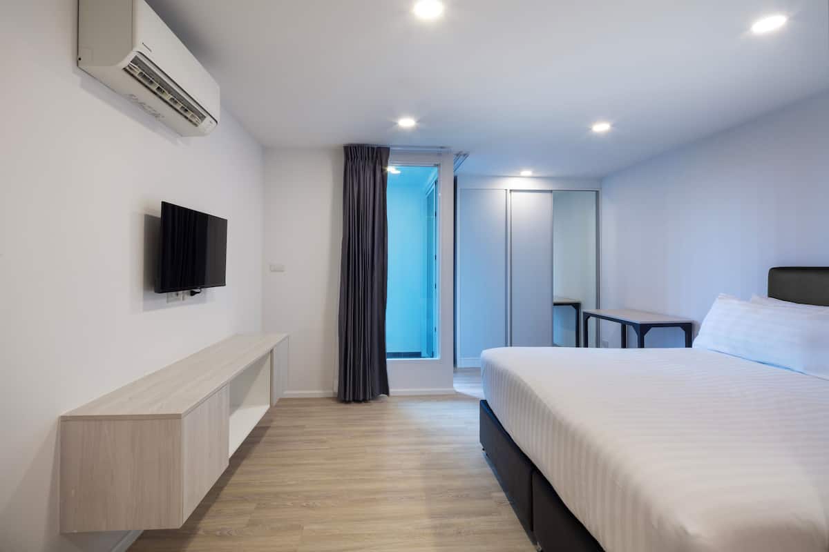 A modern hotel room with a bed, a TV mounted on the wall, a desk, and a wardrobe.