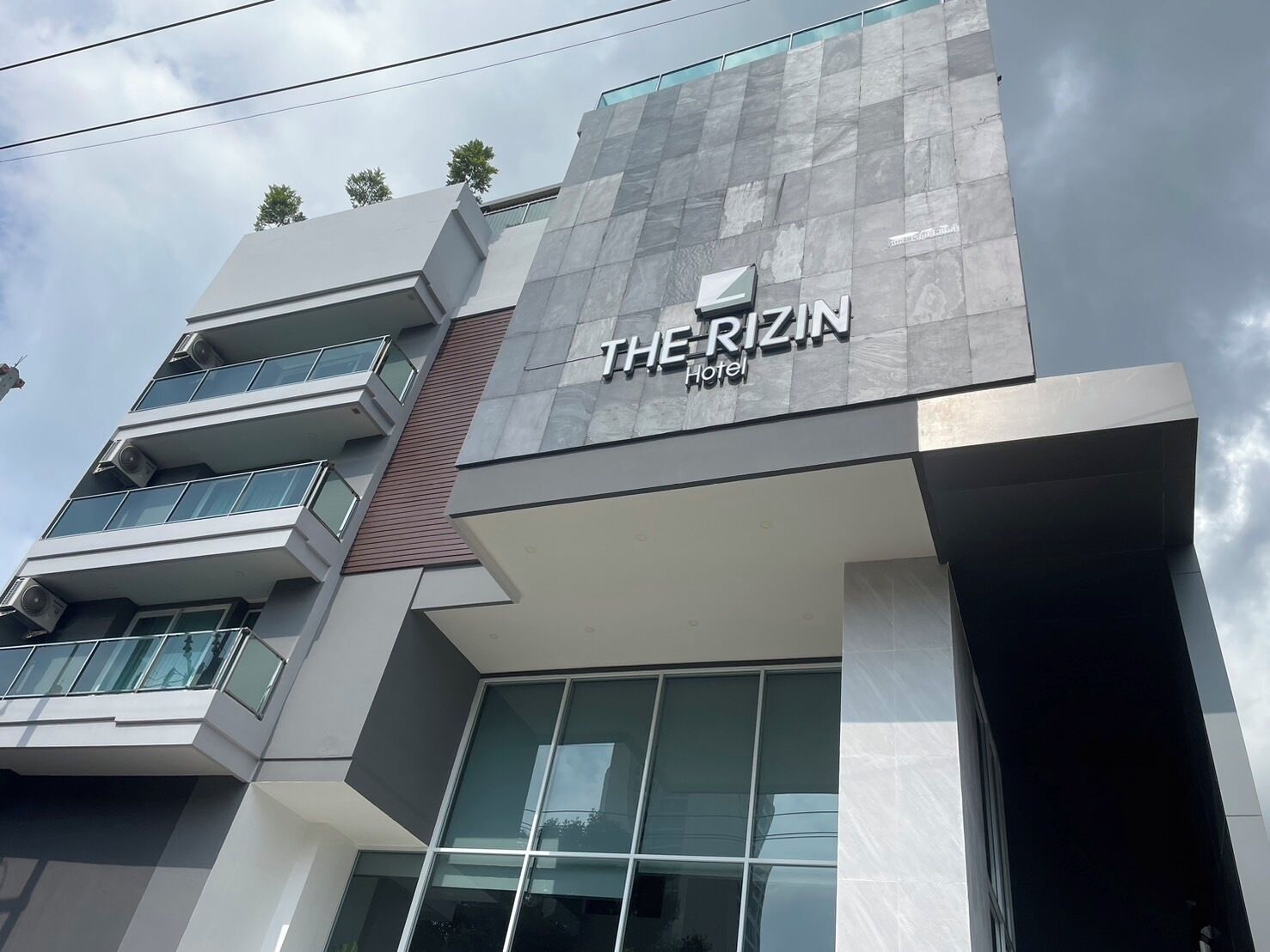 A modern hotel building with a prominent sign reading "THE RIZIN Hotel".