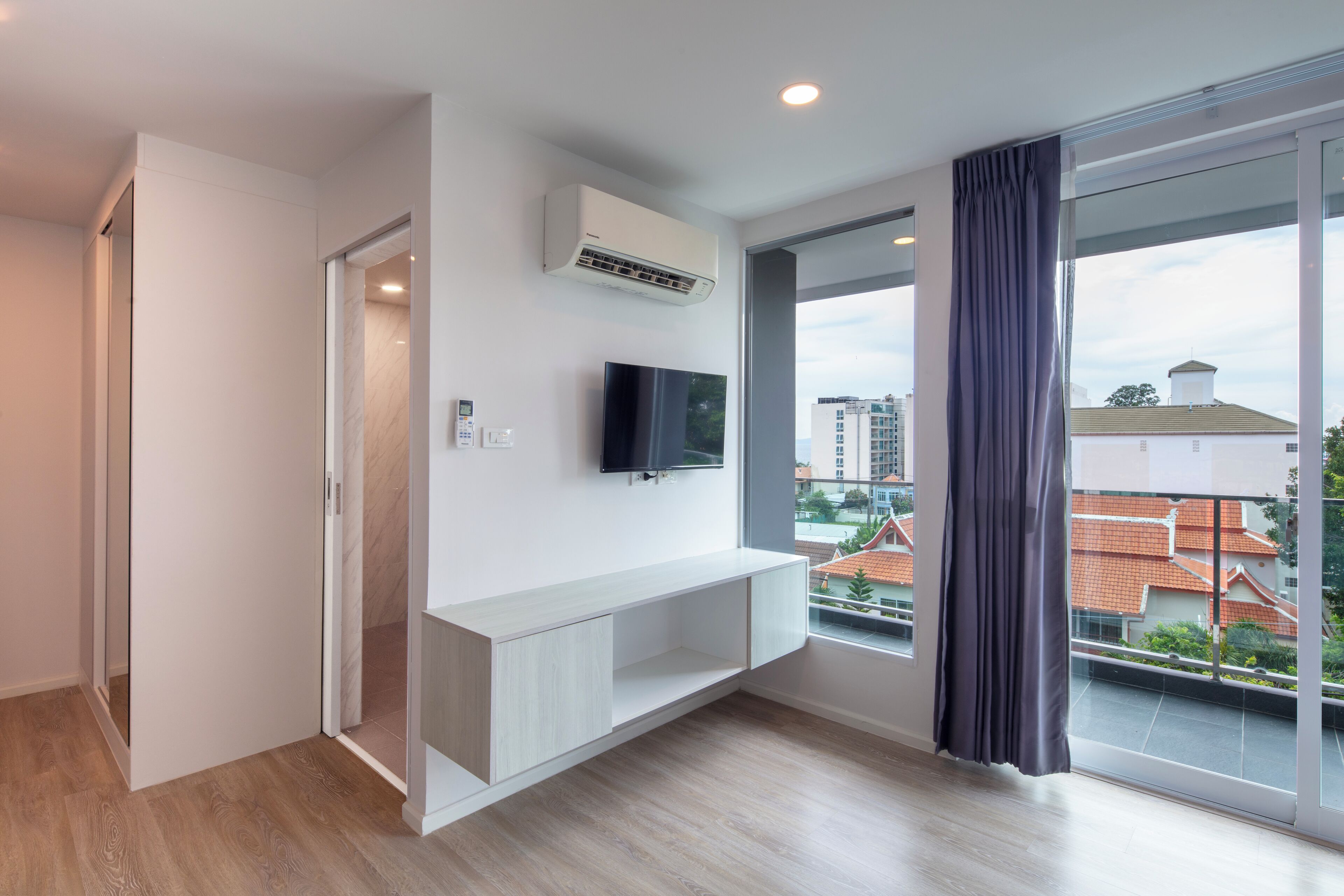 A modern room with a large window, a mounted air conditioner, a flat-screen TV, and a built-in bench.