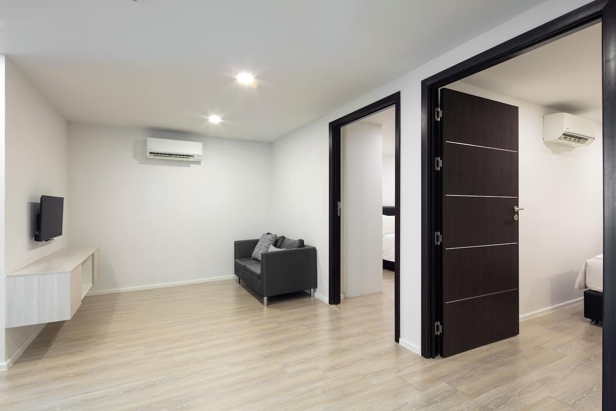 A modern living room with a grey sofa, a flat-screen TV on a white console, and an air conditioning unit on the wall.