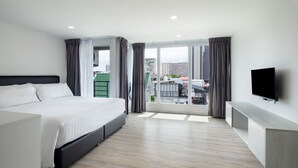 A modern hotel room with a large bed, a TV, and a balcony with a city view. - The Rizin Hotel Phratumnak (Pattaya)