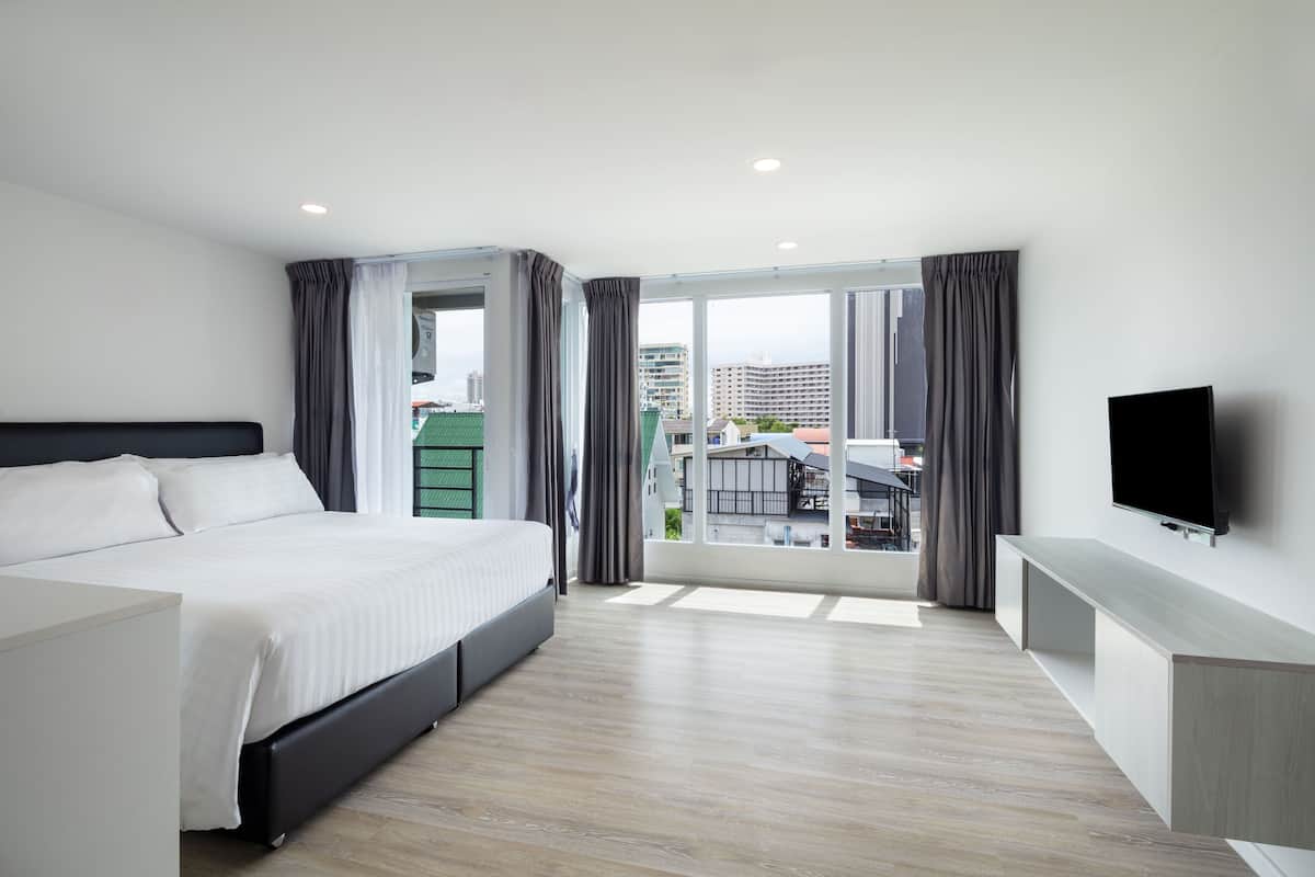 A modern hotel room with a large bed, a TV, and a balcony with a city view.