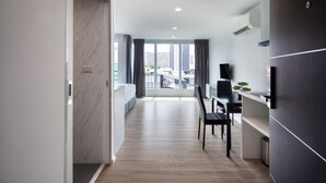 A modern kitchen with a built-in oven, a dining area with a black chair, and a view of the city through large windows. - The Rizin Hotel Phratumnak (Pattaya)