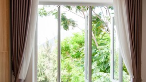 A room with a large window, a wooden chair with cushions, and curtains. -  The View Hotel (Cam Lam)
