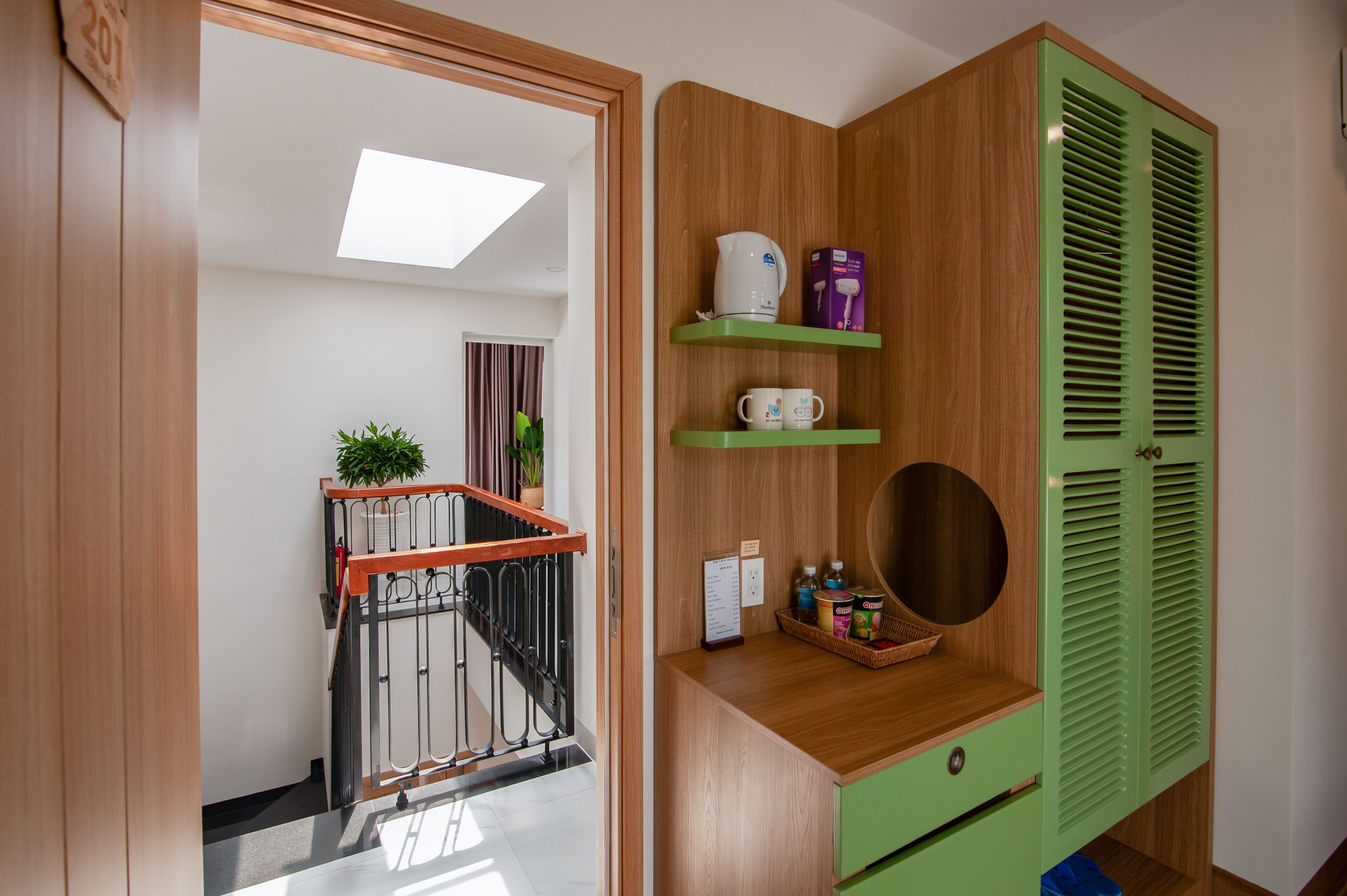 A wooden cabinet with green shutters, a small shelf with a kettle and cups, and a basket with toiletries.