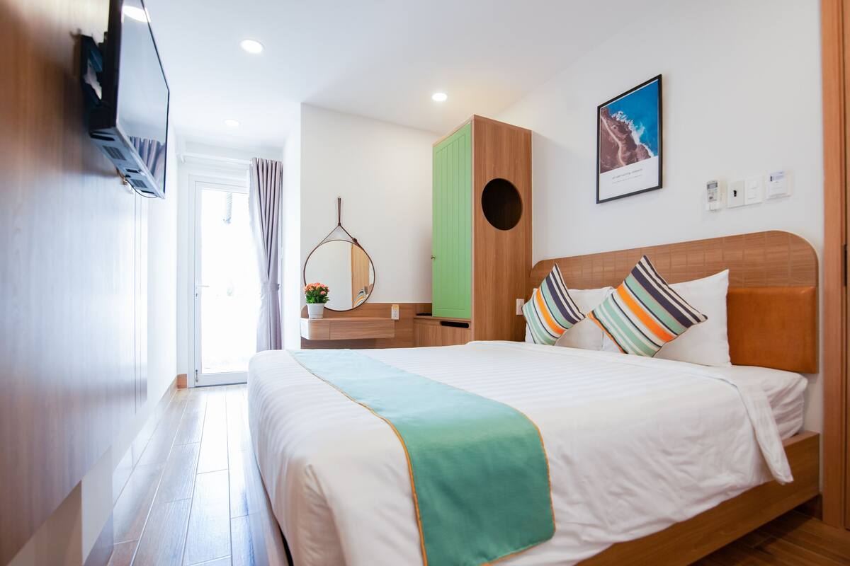 A hotel room with a bed, a TV, a green cabinet, a wooden headboard, and a framed picture on the wall.