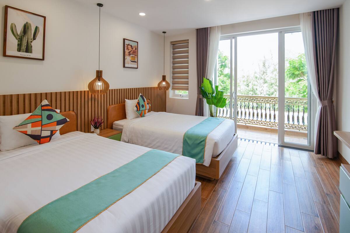 A hotel room with two beds, a balcony with a view, and a large plant.