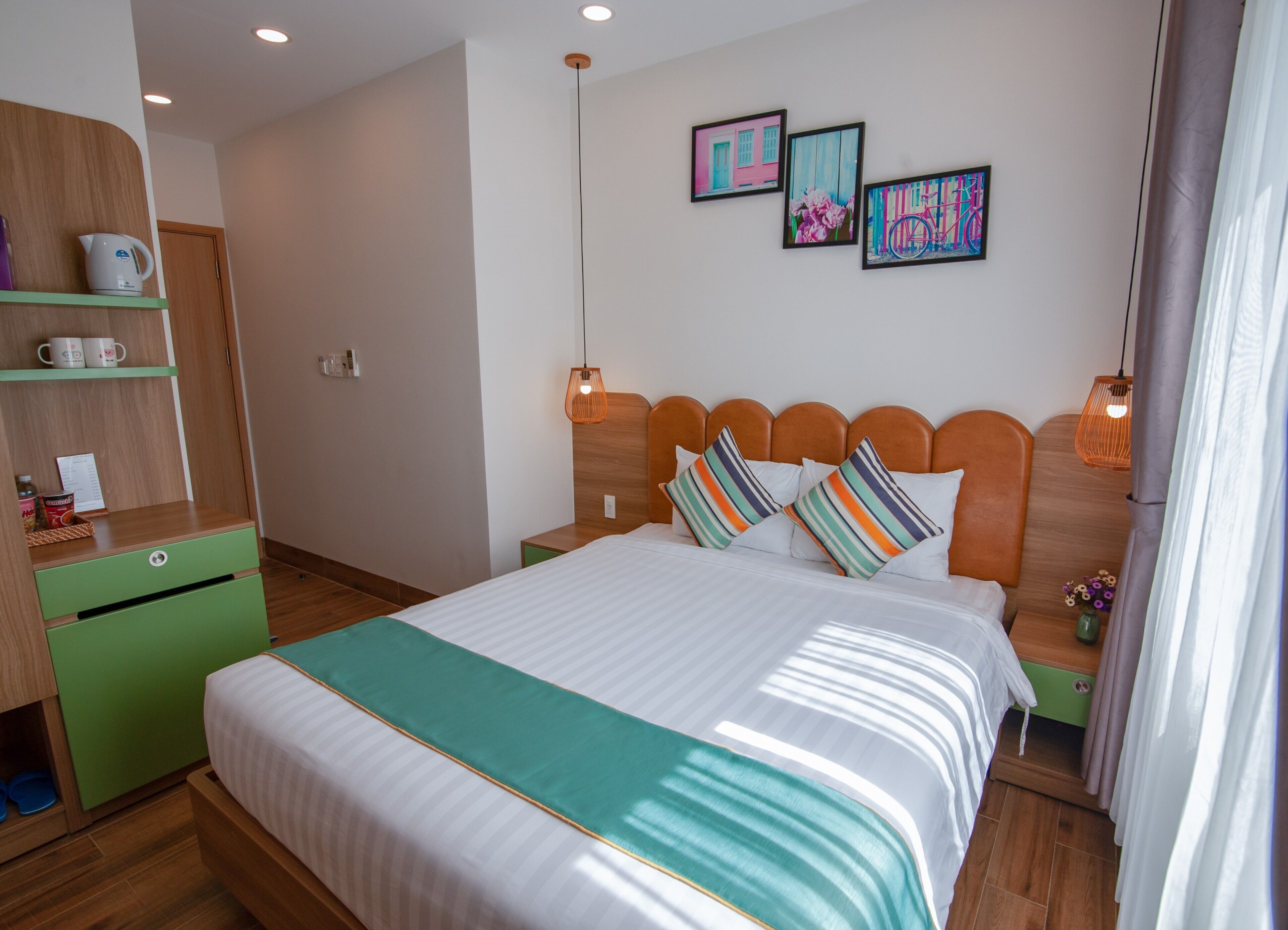 Ein ordentlich eingerichtetes Hotelzimmer mit einem Bett, einer grünen Kommode, einem Holznachttisch und einer Wand mit drei gerahmten Bildern.