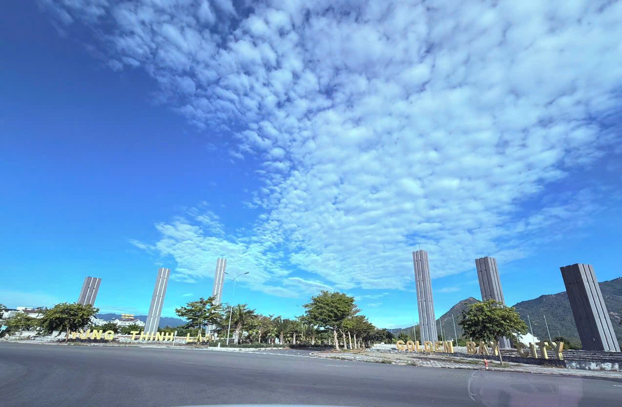 Cielo despejado con nubes, una carretera y altos edificios con señalización 'Golden Bay City'.