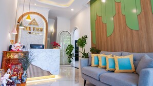 A hotel lobby with a reception desk, a sofa with cushions, and a large plant. -  The View Hotel (Cam Lam)