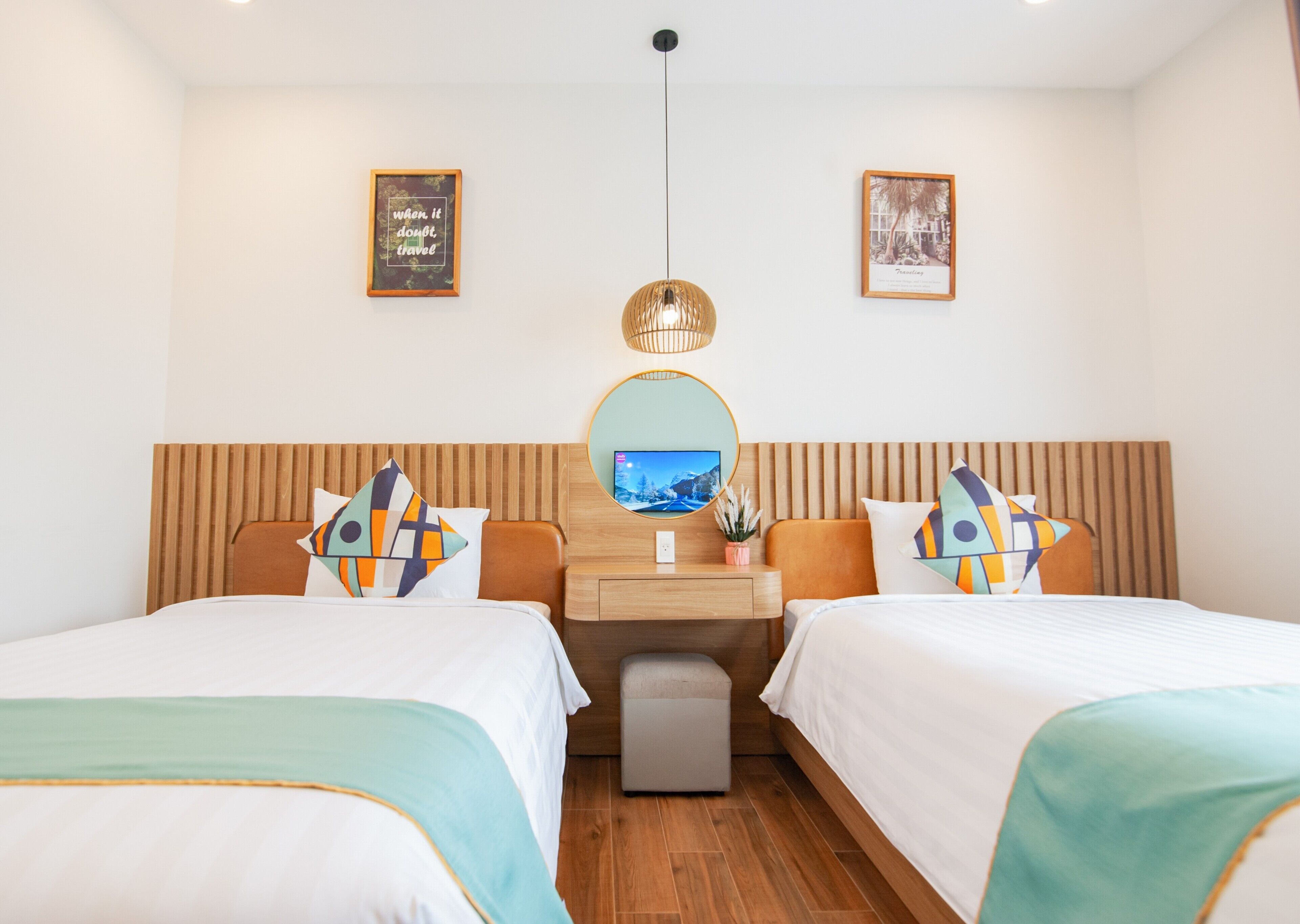 A hotel room with two beds, a wooden headboard, a desk with a mirror, and two framed pictures on the wall.