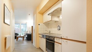 A narrow hallway leading to a kitchen with white cabinets, a sink, and an oven. There is a dining area visible in the background with a table and chairs. - Papillon Whg. 17/1, Germany (Ostseebad Boltenhagen)