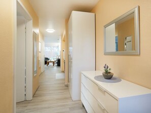 Un couloir avec une commode blanche, un miroir et une plante en pot.