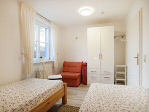 Un dormitorio con dos camas individuales, una ventana con cortinas, un armario y una mesita.