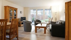 A living room with a wooden cabinet, a television, a sofa, a coffee table, and a dining area with chairs. - Papillon Whg. 17/1, Germany (Ostseebad Boltenhagen)