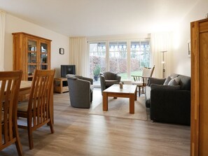 Una sala de estar con un mueble de madera, televisor, sofá, mesa de centro y un comedor con sillas.