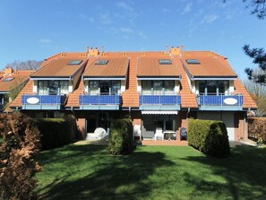 Un edificio residencial de dos pisos con techo de tejas, varios balcones y un césped bien cuidado.