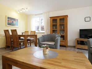 Una sala de estar con una mesa de comedor de madera, un sofá gris, un aparador de madera y un televisor.