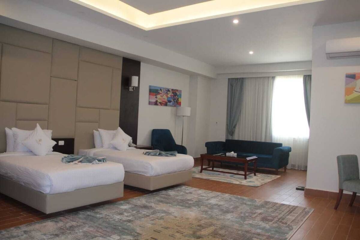 Habitación de hotel con dos camas, un sofá, una mesa de centro y un ventanal con cortinas.