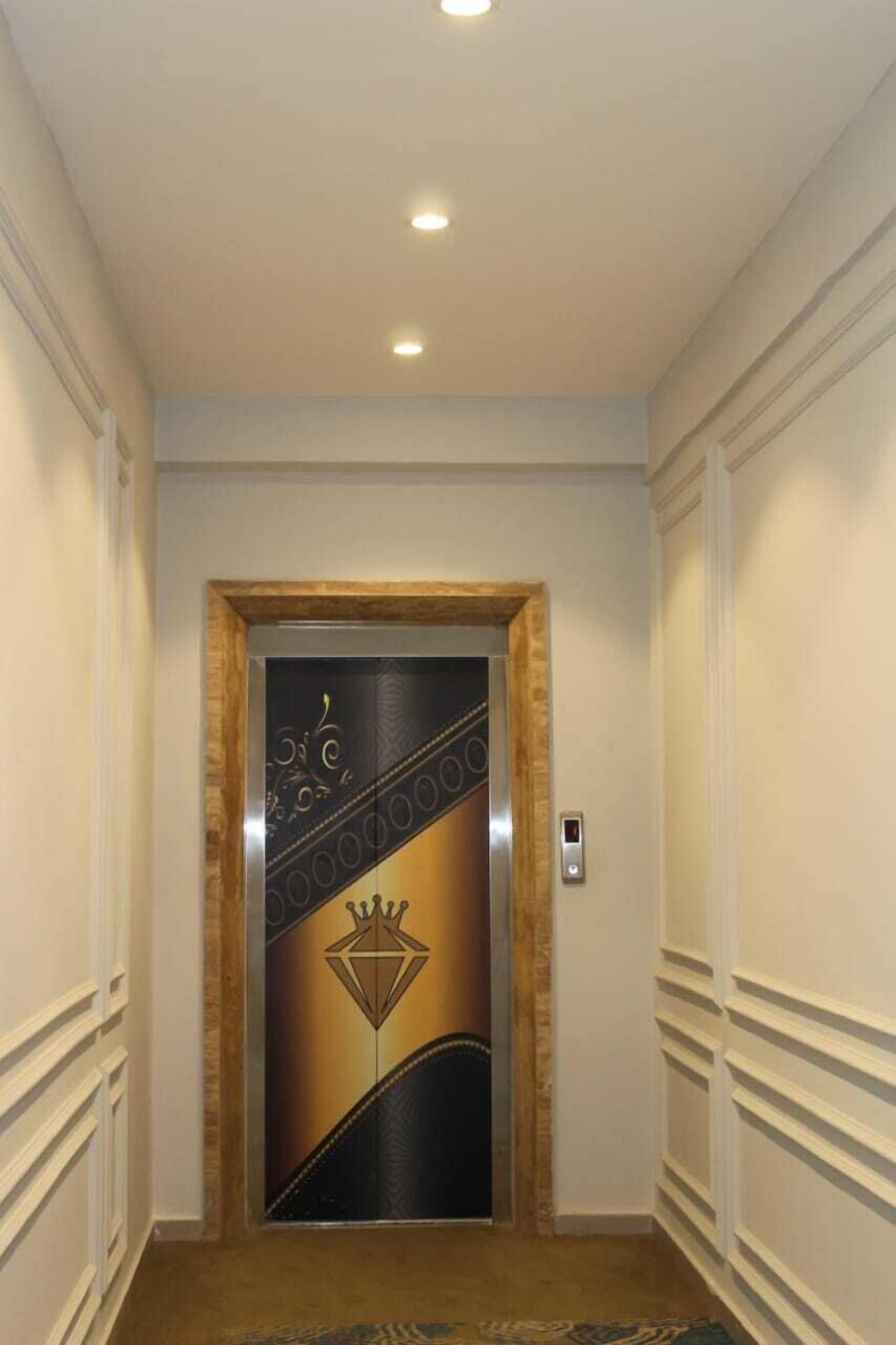 Een gang met een decoratieve liftdeur, versierd met een kroon en een diamantmotief.