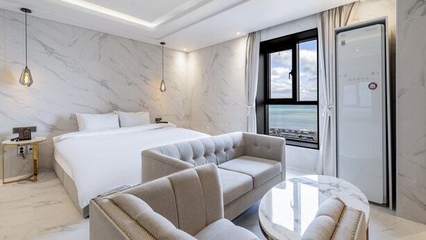 Una camera d'albergo moderna con un letto grande, due poltrone, un tavolino e vista sull'oceano dalla finestra.