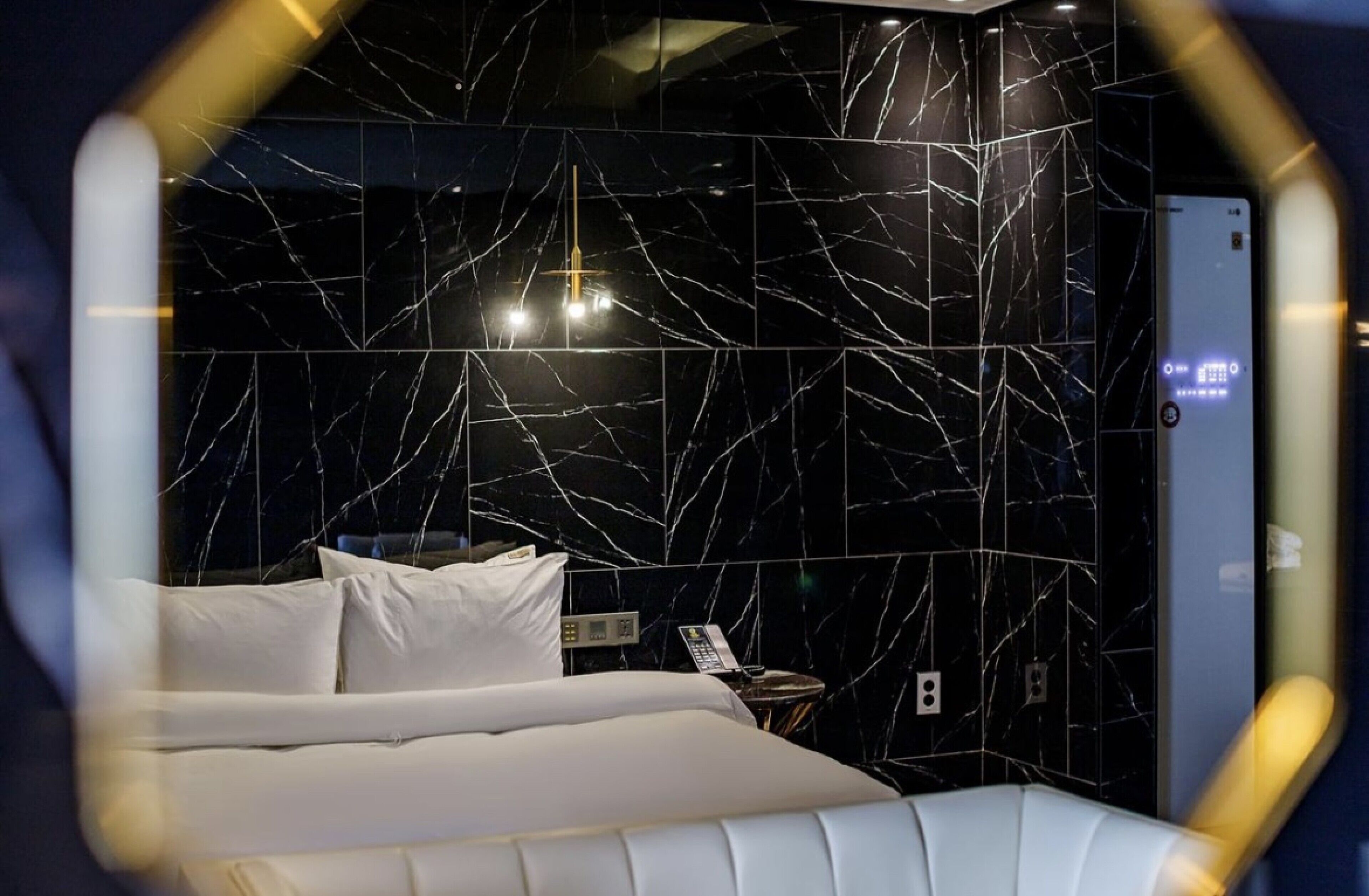 Ein modernes Hotelzimmer mit einer Wand aus schwarzem Marmor, einem weißen Bett und einem Nachttisch mit Telefon.