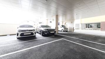 Un estacionamiento con tres autos, un edificio de amplios ventanales y techo de baldosas.