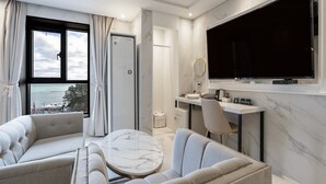 Una moderna camera d'albergo con una televisione grande, sedute confortevoli, una scrivania e vista sul mare.