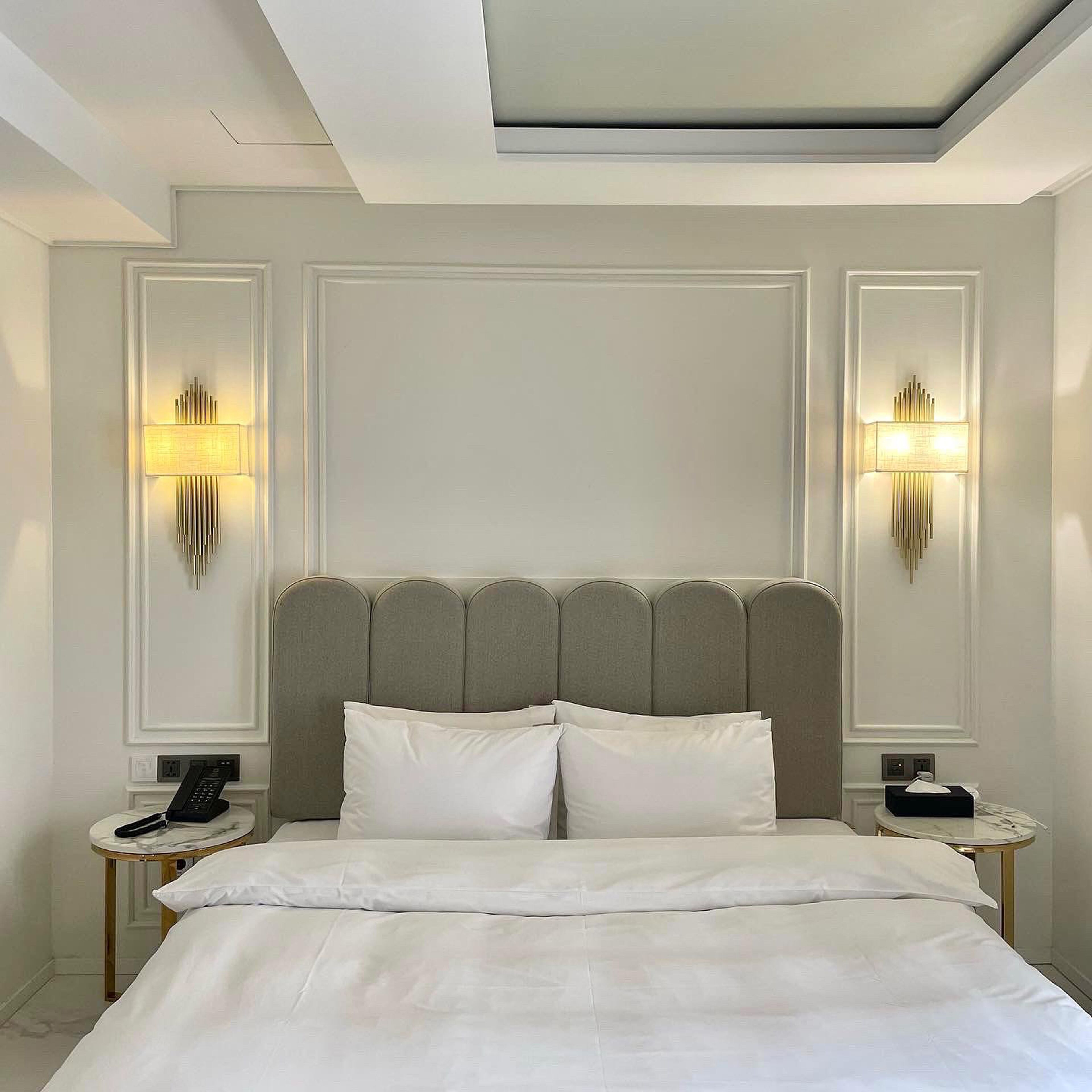 Habitación de hotel con una cama grande, dos mesitas de noche, un cabecero moderno e iluminación empotrada en la pared.