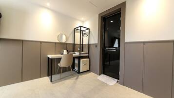 Quarto de hotel pequeno com escrivaninha, cadeira e guarda-roupa.
