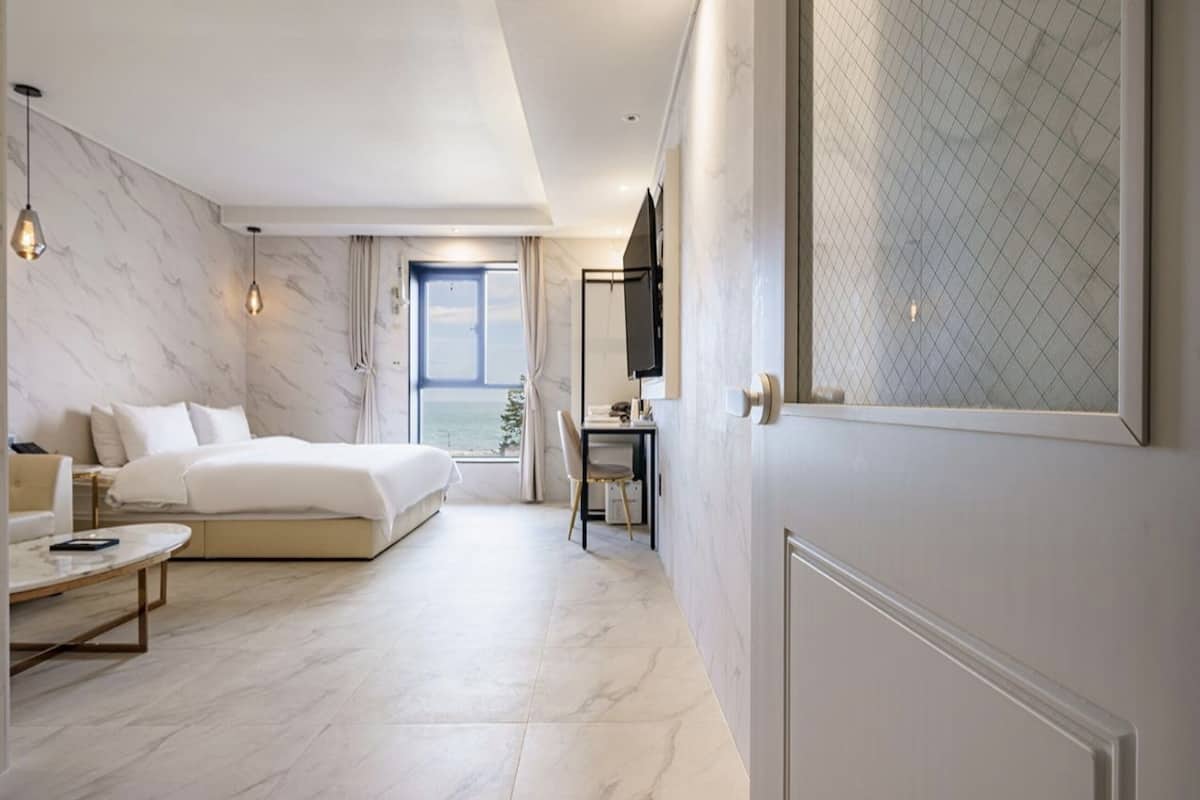 A modern hotel room with a large bed, a desk, and a view of the sea.