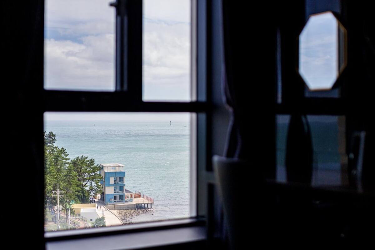 A view through a window with a view of the sea and a building with a red roof.
