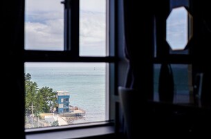 Vista a través de una ventana que da al mar y un edificio con techo rojo.