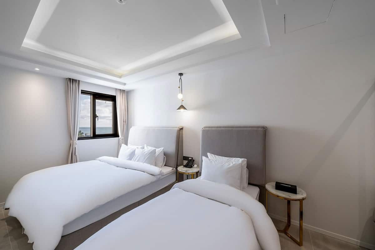 A hotel room with two beds, a small bedside table with a phone, and a window with curtains.
