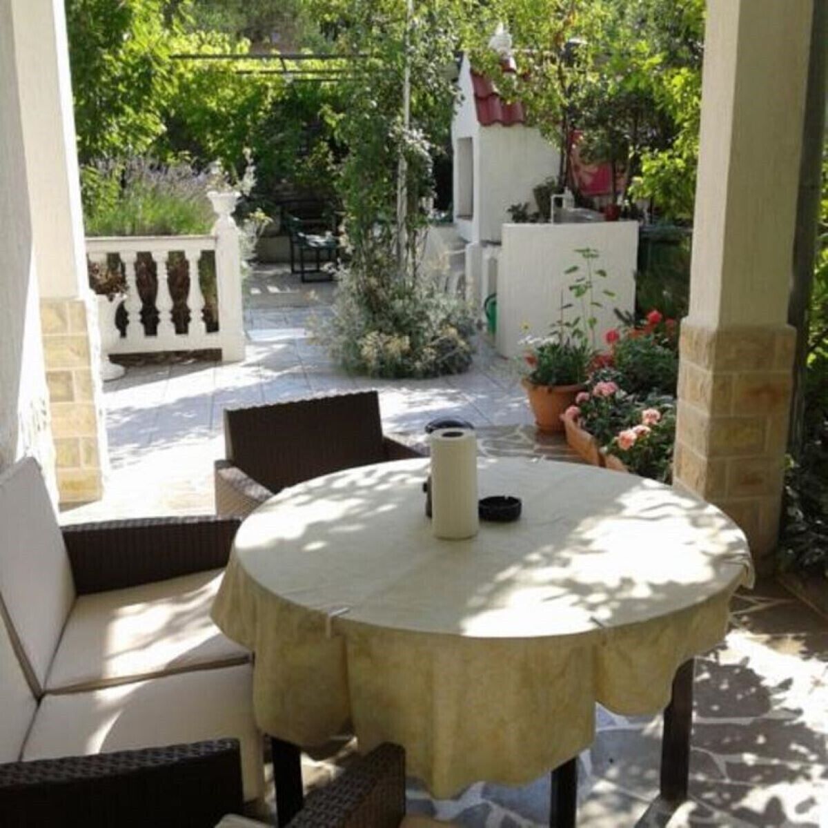 A covered patio with a round table, wicker chairs, and potted plants.