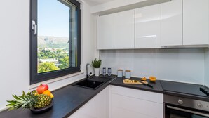A modern kitchen with white cabinets, a black countertop, a stainless steel oven, and a window with a city view. - Apartment Luni (Dubrovnik)
