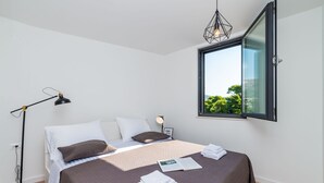 A neatly made bed with a brown bedspread, white pillows, and a bedside lamp. - Apartment Luni (Dubrovnik)