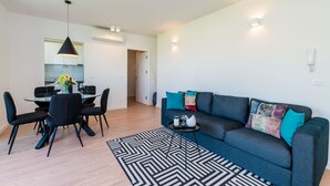 A modern living room with a dark blue sofa, black chairs, a glass dining table, and a black and white rug. - Apartment Luni (Dubrovnik)