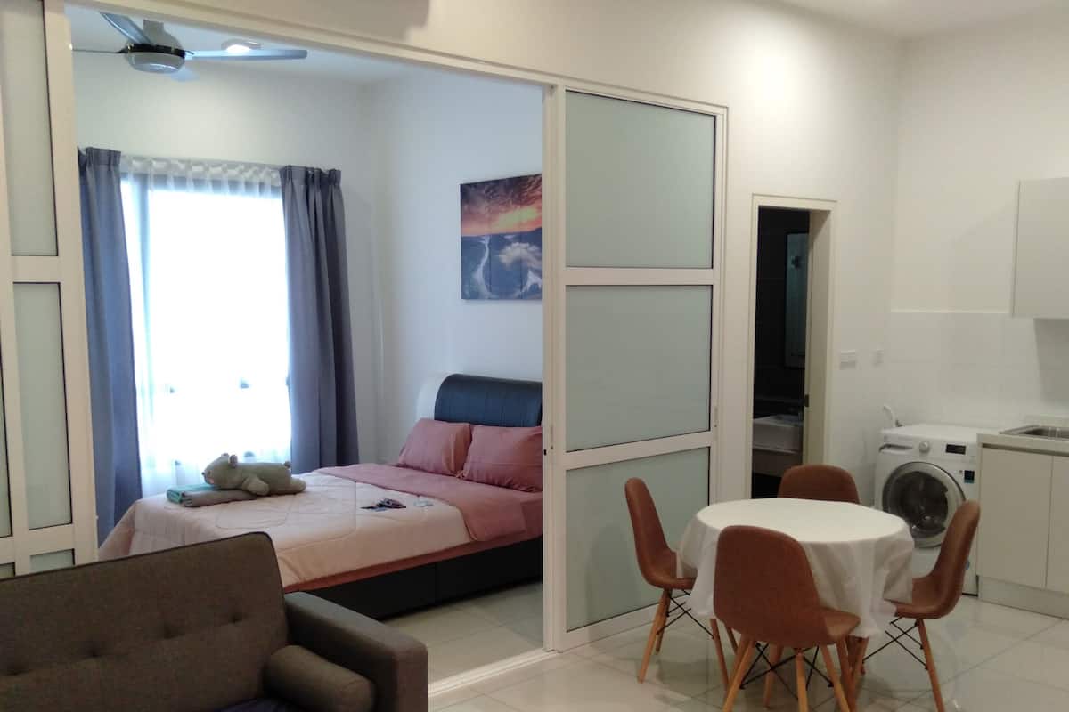A bedroom with a bed, a sofa, a dining table with chairs, a washing machine, and a painting on the wall.
