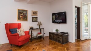 Una sala de estar con un sillón rojo, un televisor, cuadros enmarcados y un aparador de madera.