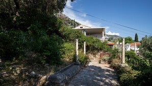 Un sendero de piedra que conduce a una casa con techo de tejas rojas, rodeada de abundante vegetación y un cielo azul despejado.
