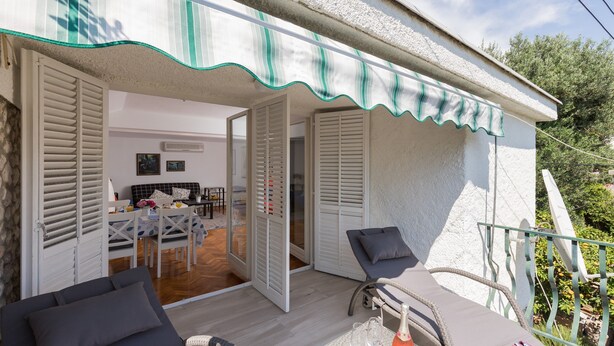 A cozy outdoor seating area with a table and chairs, a bicycle, and a balcony with a railing. - Apartment Dubo (Dubrovnik)