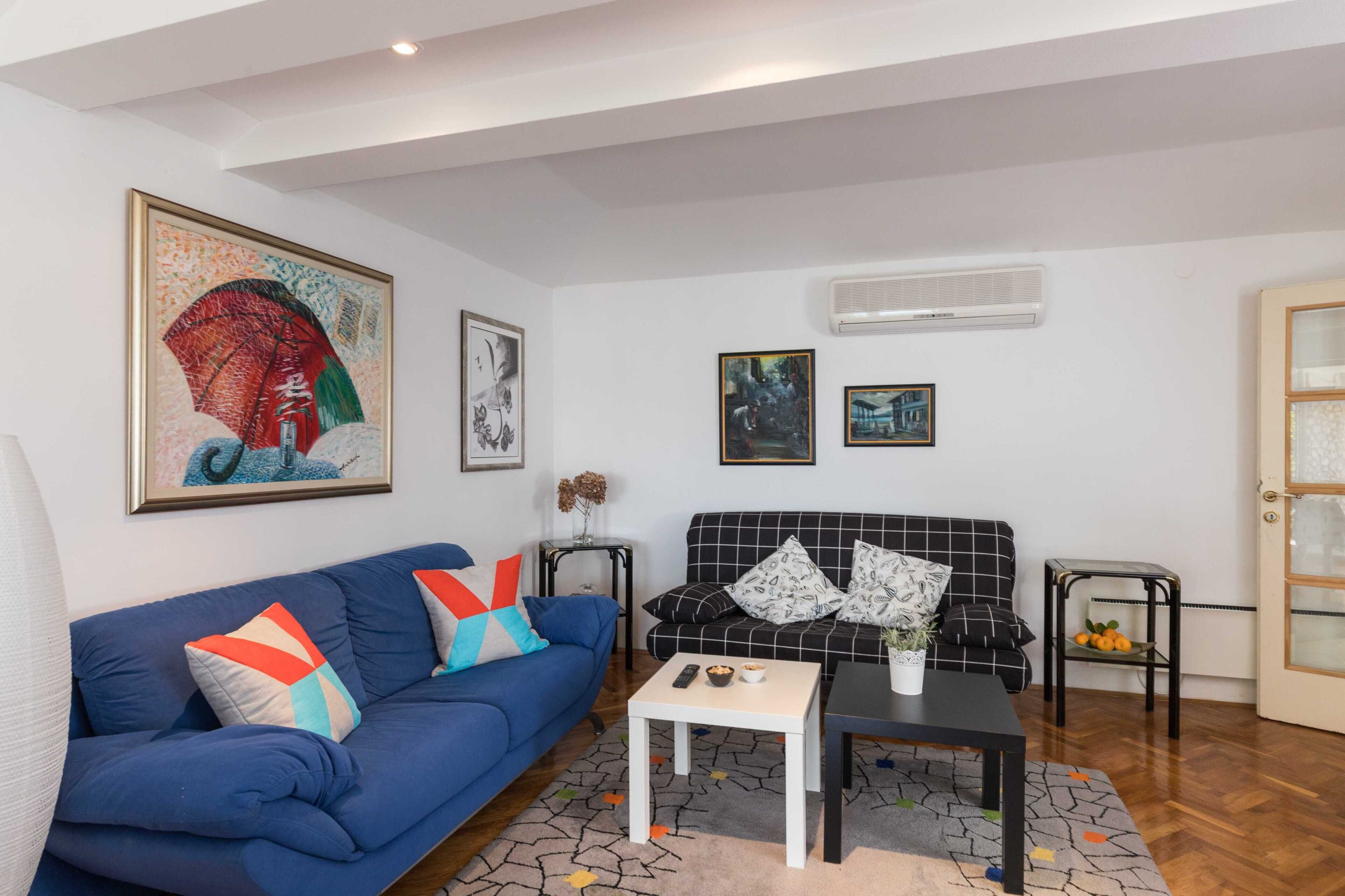 A living room with a blue sofa, a black sofa, a coffee table, and a small side table with a vase.