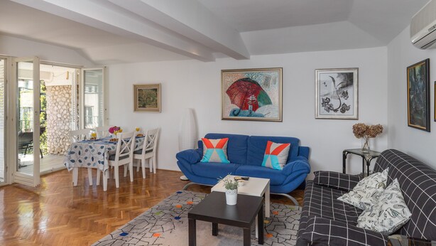 Una sala de estar con un sofá azul, un sofá negro, una mesa de comedor con sillas y una mesa de centro.