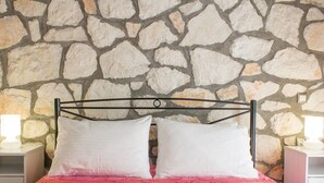 A bed with a stone wall background, two white pillows, and a pink patterned bedspread. - Harmony Villa — Stone Retreat in Zakynthos Marine Park, 2 km to Laganas Beach (Mouzaki)
