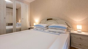 A neatly made bed with a headboard, a bedside table with a lamp, and a wardrobe with a mirror. - Apartment Gordana (Split)