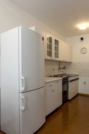 A kitchen with white cabinets, a white refrigerator, a stove, and a clock on the wall.