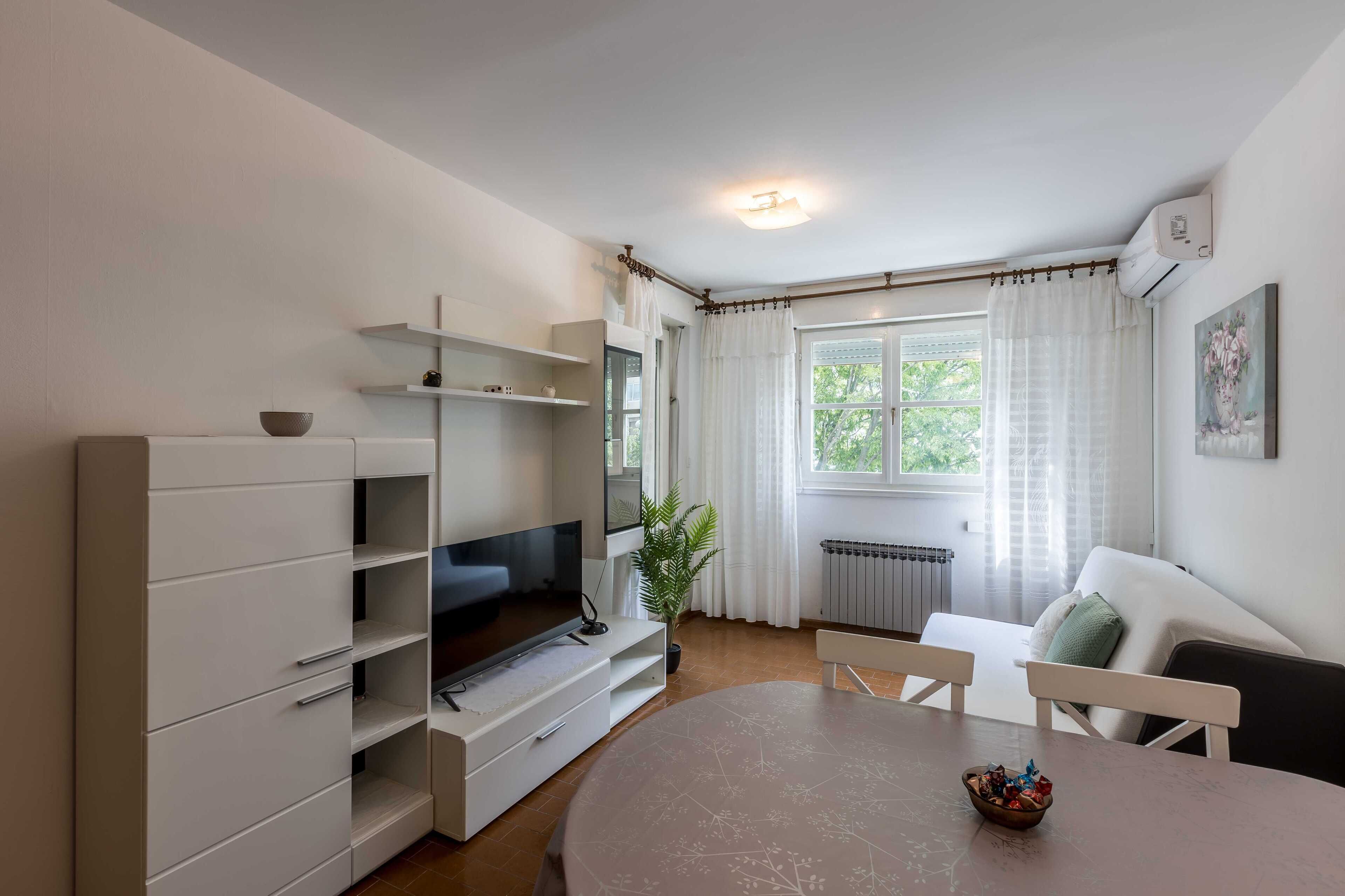 A modern living room with a flat-screen TV, a dining table, and a sofa.
