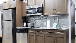 A modern kitchen with stainless steel appliances, wooden cabinets, and a tiled backsplash. - Hotel Manhattan, BW Signature Collection (New Caney)